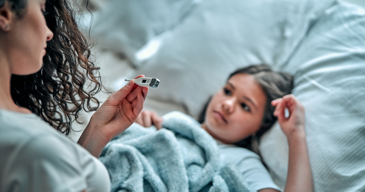 Parent checking phone next to a child resting with a thermometer and medicine bottle on the nightstand